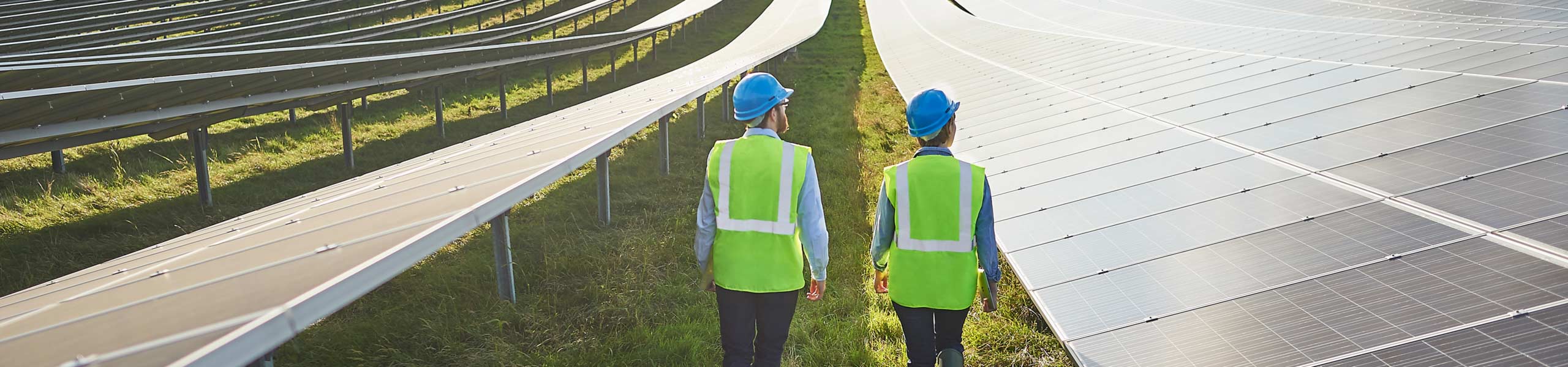 Young male and female surveying engineers in safety wear walking through solar farm.