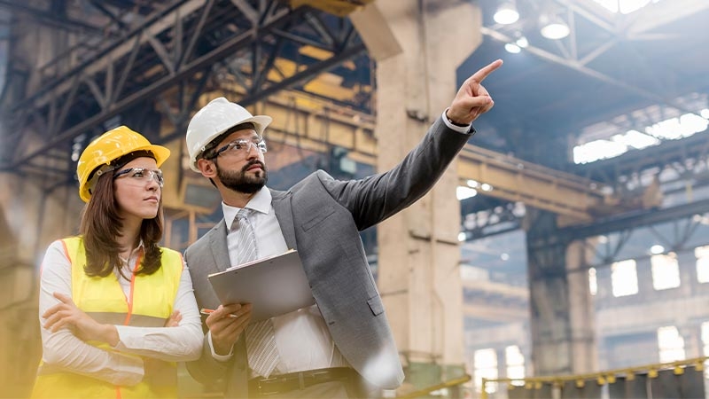 A person and person wearing hardhats and holding a tablet