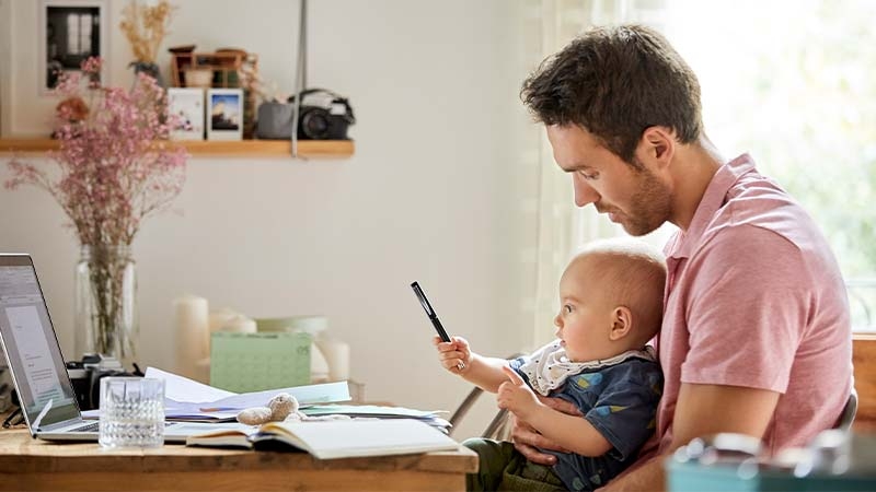 A person holding a baby while looking at a cell phone