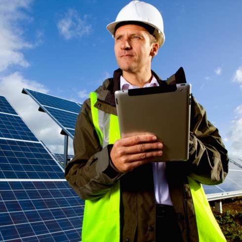 Engenheiro com tablet digital em pé na frente de painéis solares, gestão de energia.