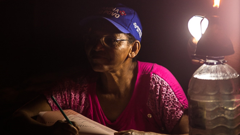 An old lady wearing a cap writing something in a notebook