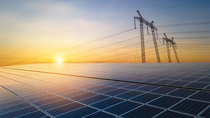 Solar panels and power lines in front of a sunset