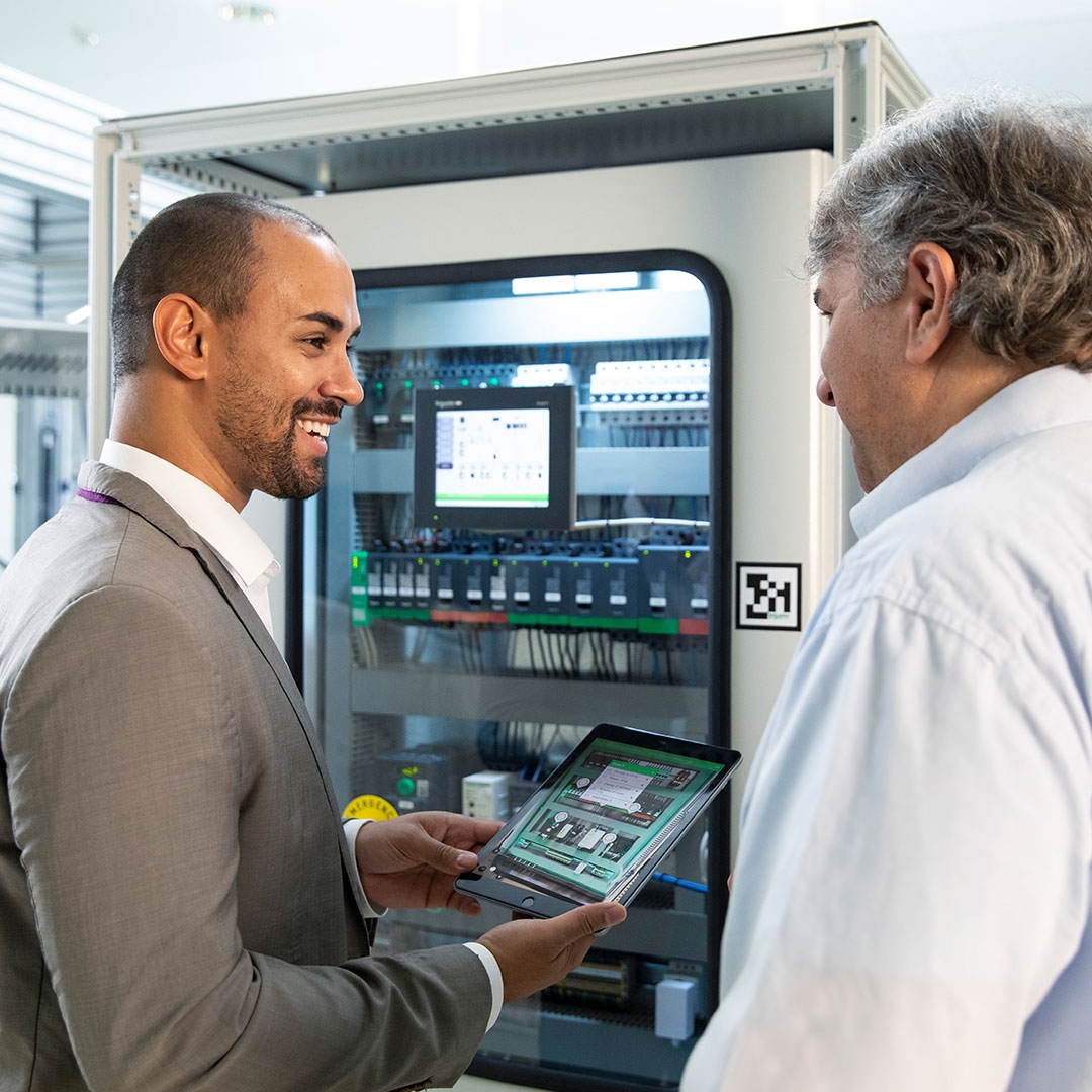 A man in suit holding a digital tablet talking to another man standing by his side