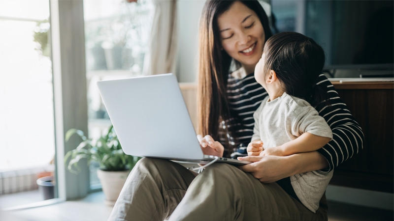 The lady is working on her laptop while the child sits on her lap