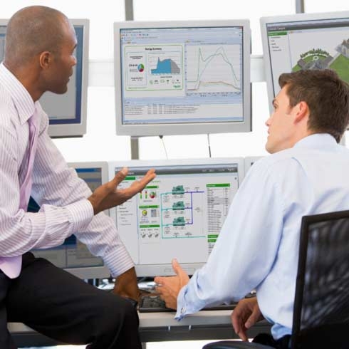 obchodníci před monitory s monitorovacím softwarem Schneider Electric prohlížejí zprávy o udržitelnosti a analýzu big dat.