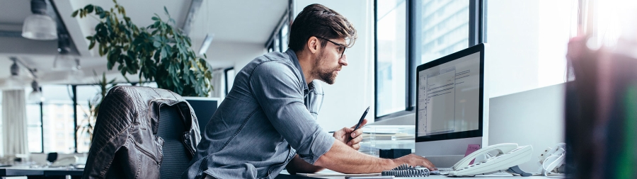 A man sitting on his desk and working on his desktop computer in the office