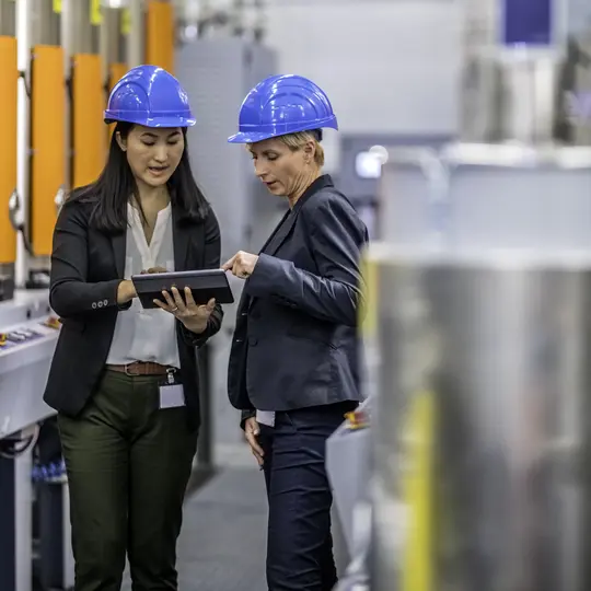 Asian female engineer using a digital tablet to explain the production process in a factory to a female company board member