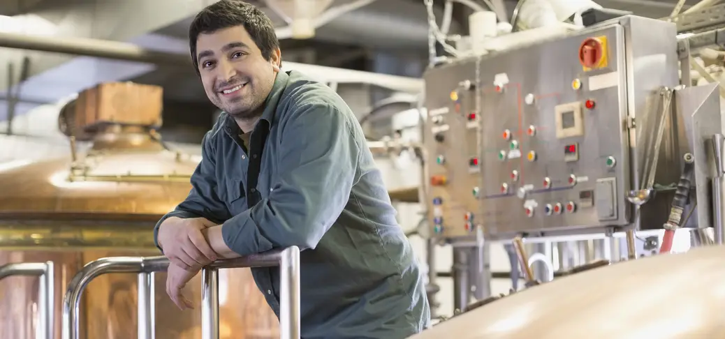 Portrait of confident brewery worker near copper stills.