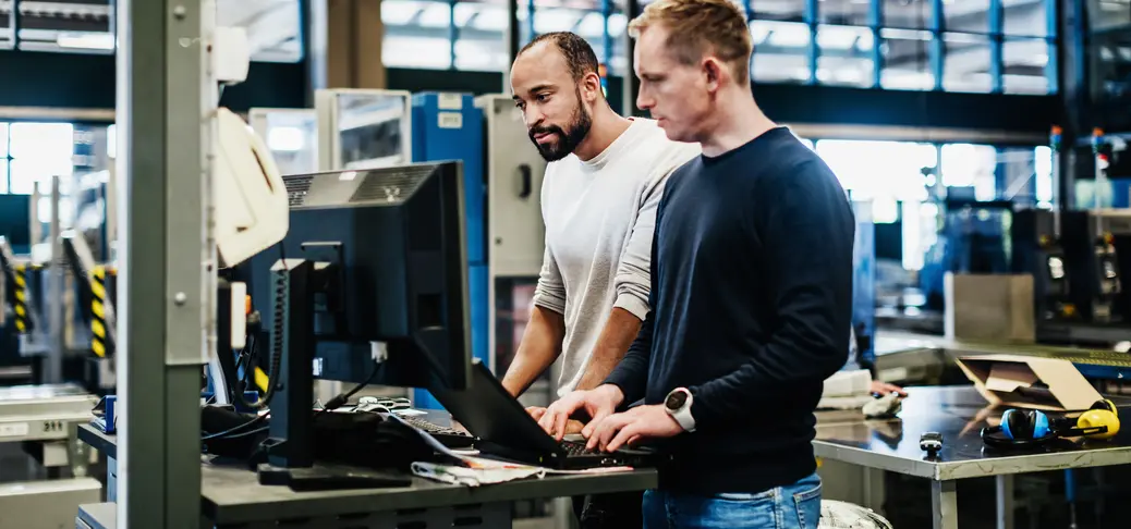 Two engineers concentrating while using computers together on a print factory machine floor