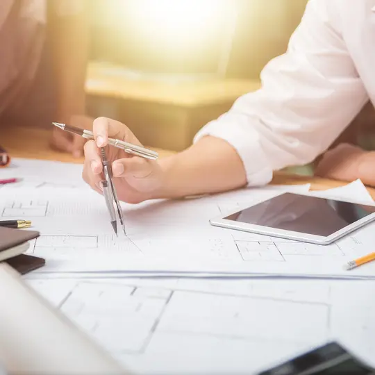 Hands of architect or engineer using drawing compass with blueprint on desk in office