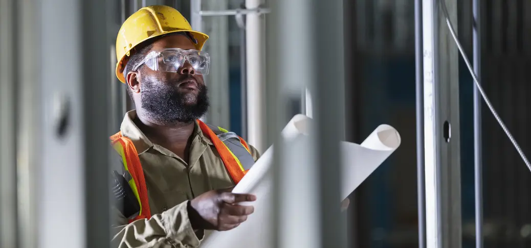 Construction worker with plans, examining structure.