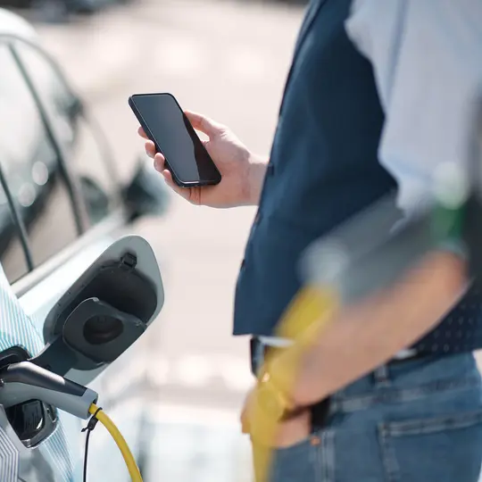 Young man is holding a phone while electric car charged