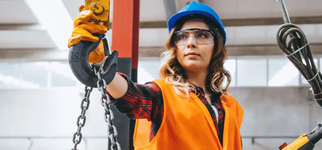 Skilled young heavy industry engineering worker woman holding crane hook button working with safety workwear