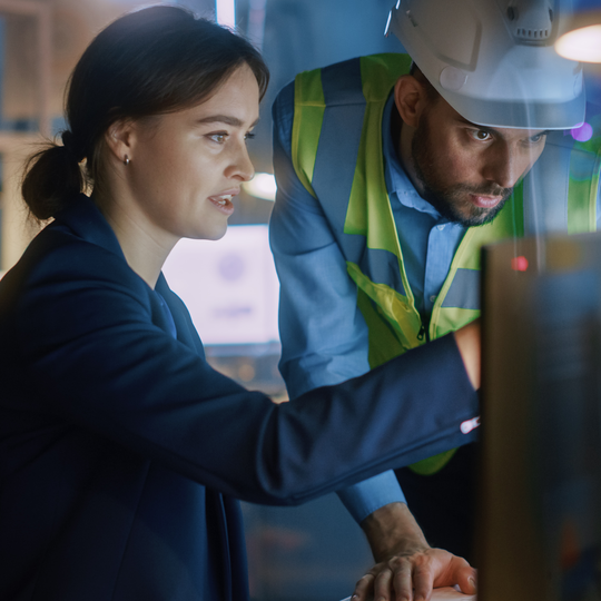 Modern factory office: male project manager talks to a female industrial rngineer who works on computer