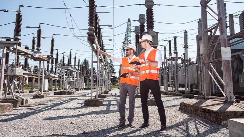 A group of men in orange vests and helmets standing in front of power lines