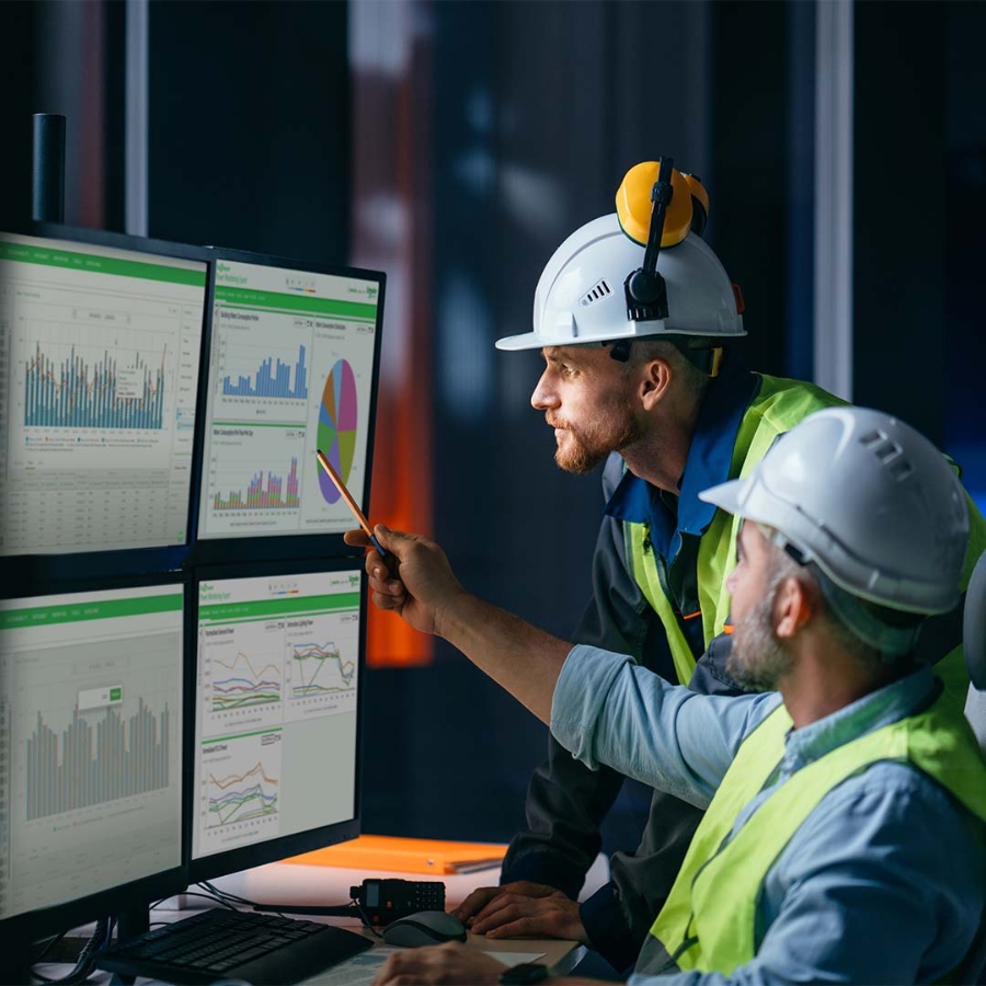 A group of men wearing hard hats and standing in front of computer screens