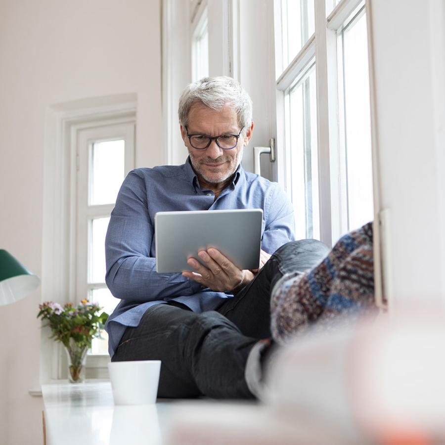 Mature man at home sitting at the window using tablet