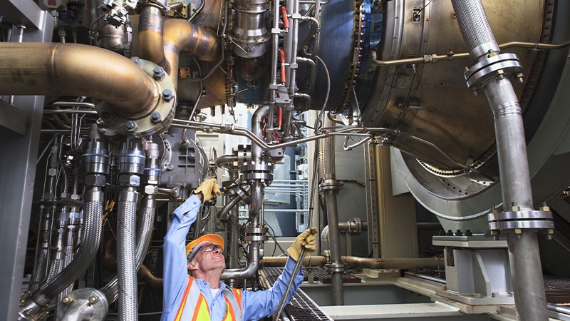 Engineer examining instrumentation cables at fuel injection stage of gas turbine which drives generators in power plant while turbine is powered down