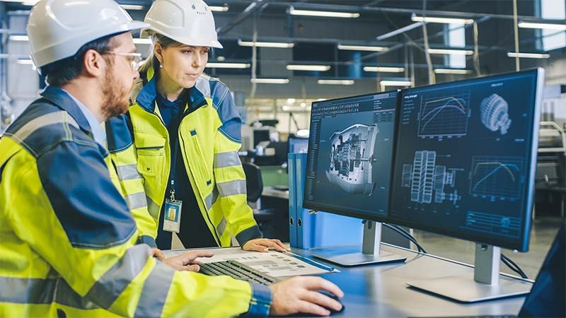 A person and person in hardhats looking at computer screens