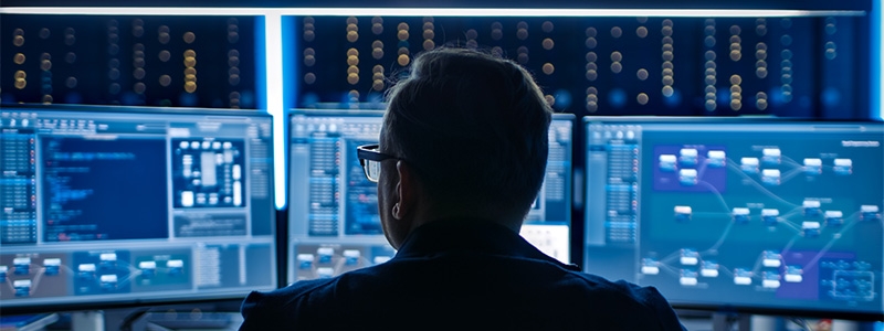 cybersecurity specialist working on computer with three displays ensuring security of smart airport digital environment