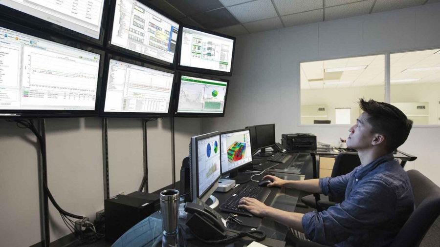 A male employee working in a control room having several monitors on wall