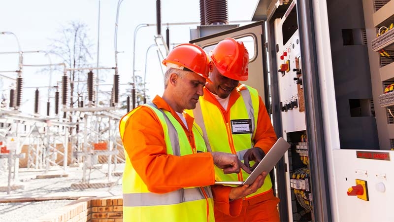 Men in orange vests and orange hard hats looking at a computer