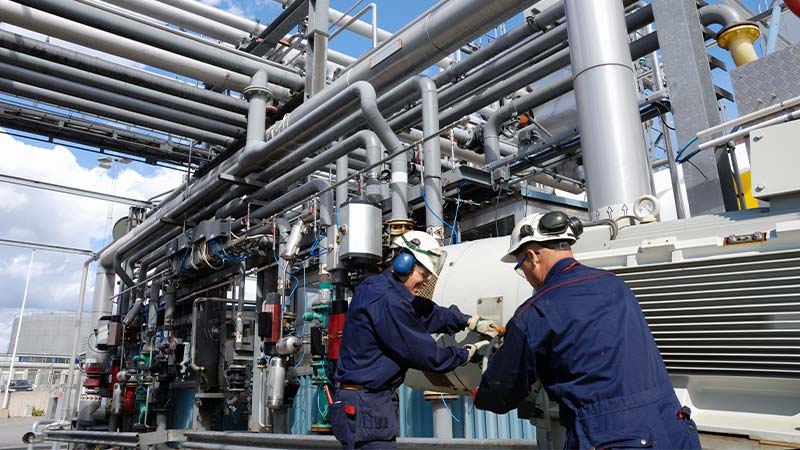 Men in blue overalls and helmets working on a machine