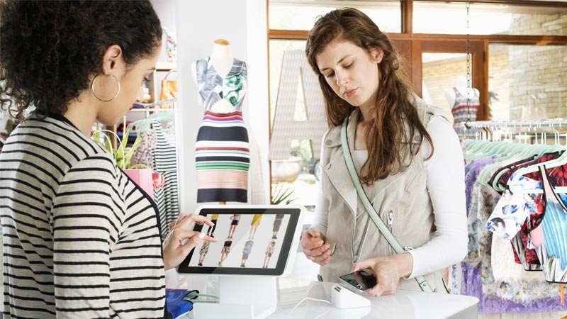 Woman shopping in clothing store paying with smart phone