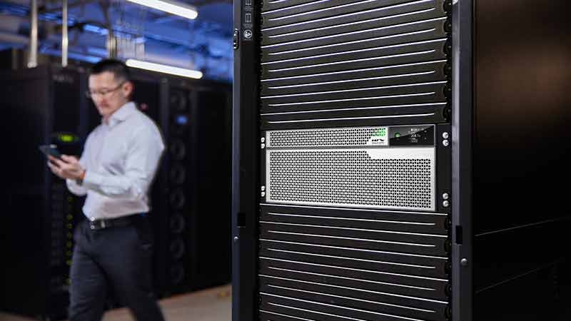 IT Professional walking by an APC Smart-UPS Ultra 4U 10kVA installed in an APC NetShelter rack.