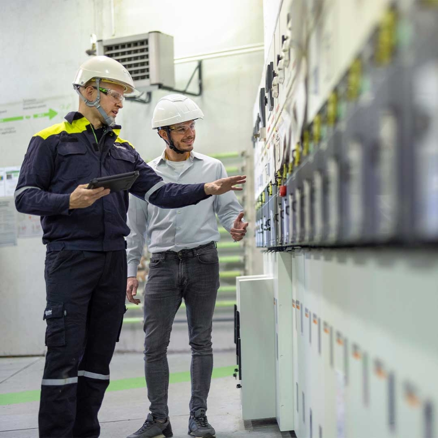 A person in hardhats standing next to a person in a factory