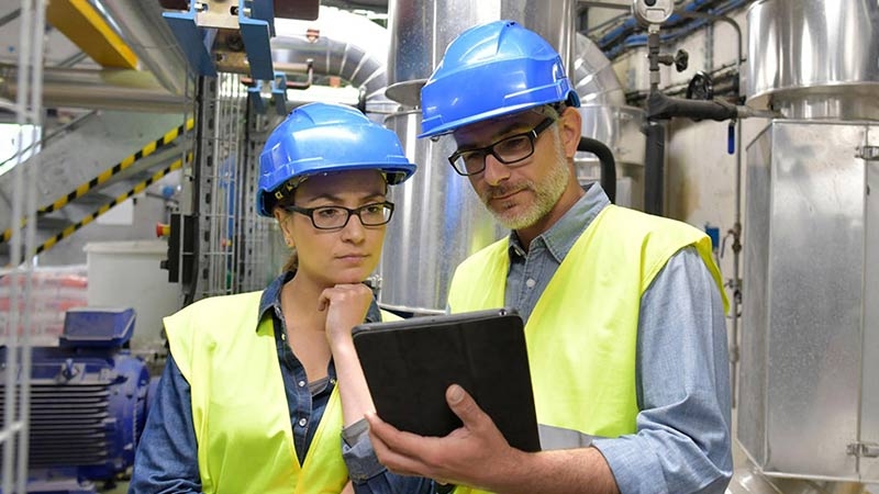 two men blue hard hats discussing clipboard