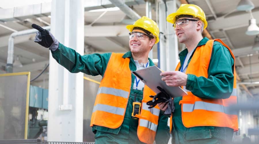 Workers in protective workwear talking with clipboard in factory