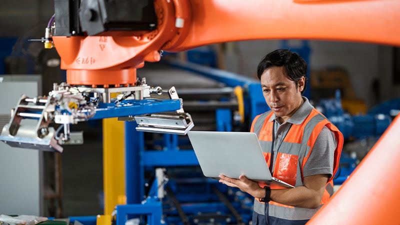 Engineer programming a robot to increase productivity of EV battery manufacturing processes