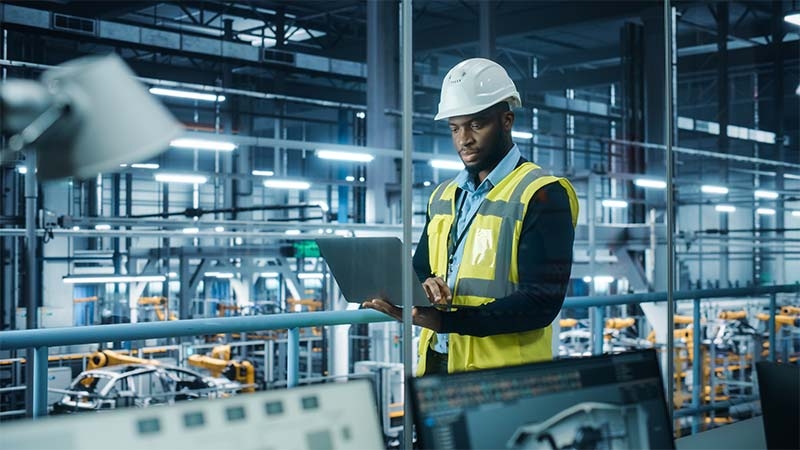 A person in a safety vest and hardhat holding a computer