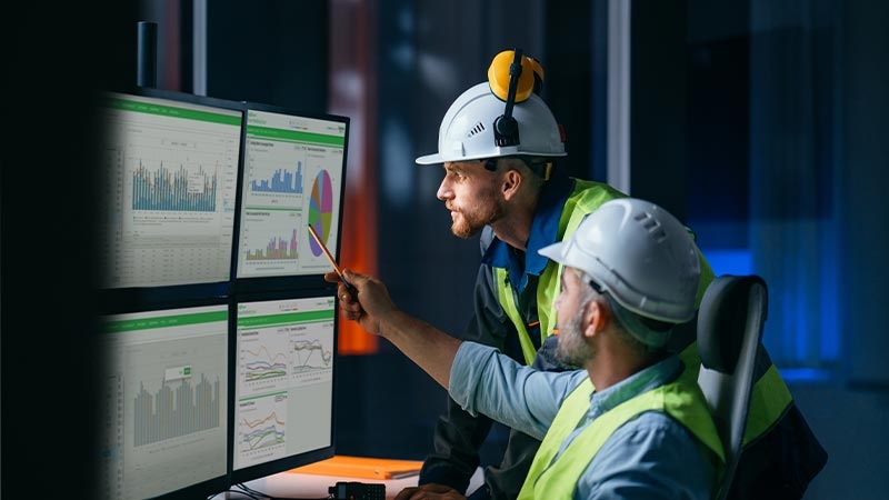 A group of men wearing hard hats and standing in front of a computer