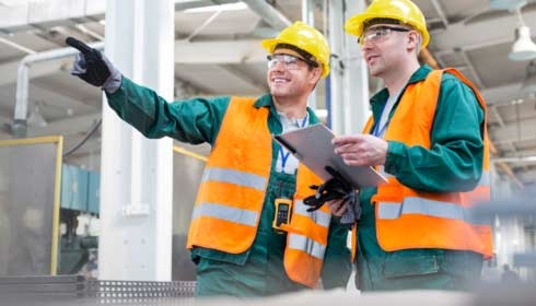 Workers in protective workwear talking with clipboard in factory