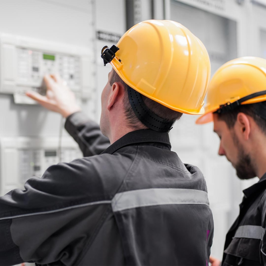 Men wearing hardhats and working on a control panel