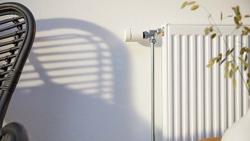 Wiser radiator thermostat mounted on element sitting on white wall.