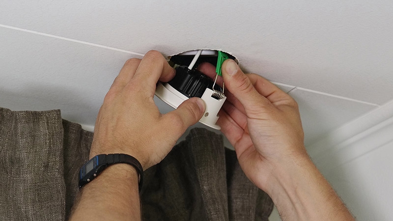 Electricians hands installing downlight in ceiling