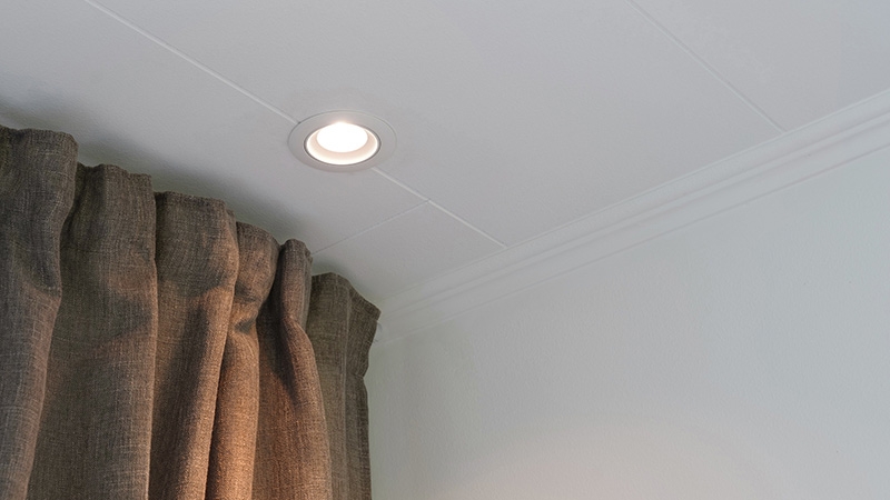 Lit white downlight mounted in ceiling next to a curtain.