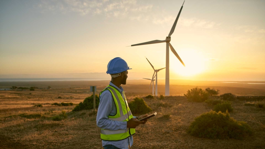 A person in a hard hat and vest standing in front of windmills