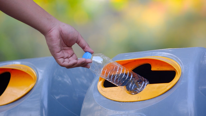 A hand throwing a plastic bottle into a trash can