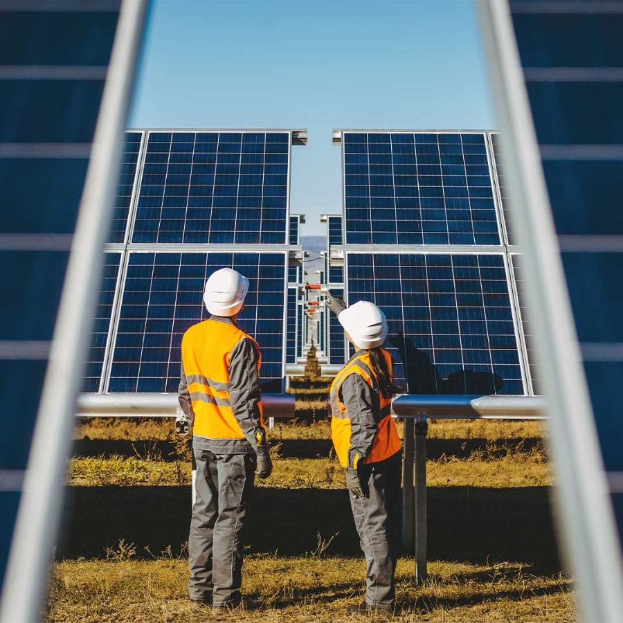 A couple of men in orange vests and helmets standing in front of solar panels