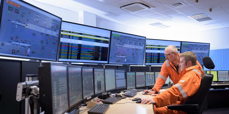 men in orange jackets looking at computer screens