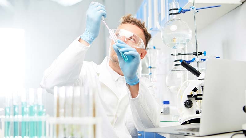 A person in a lab coat and gloves holding a pipette