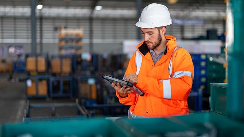 A person in an orange jacket and white hard hat using a tablet