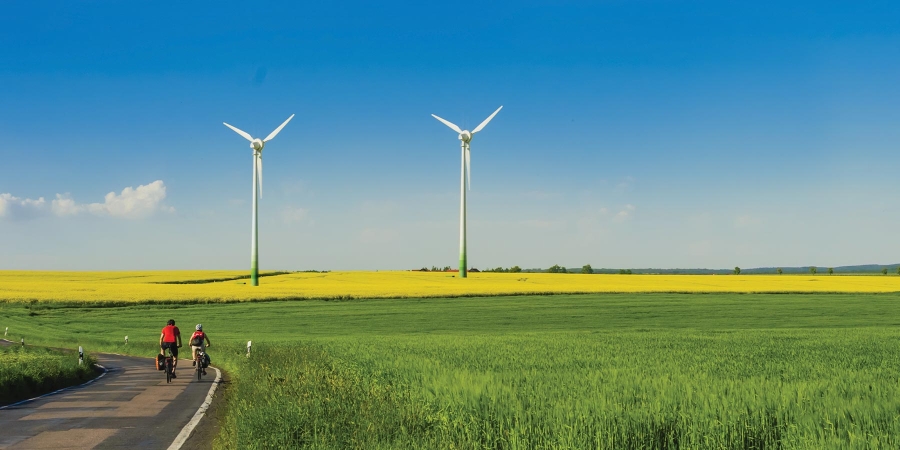 man cycling in front of wind mill and field