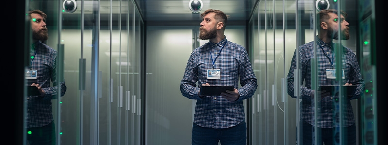 a men with digital laption standing in the data center server room checking the performance of the equipment