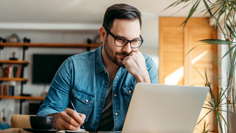 Man sitting in front of a laptop holding a pen