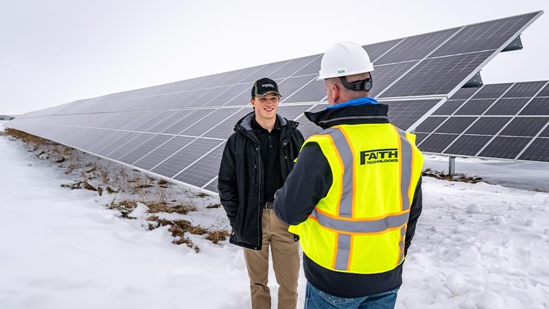 A person in a yellow vest talking to a person in a white helmet